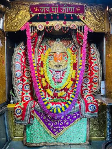 Garbhagriha of Jeen Mata Temple with the Goddess under a 'Jai Maa Jeen' canopy, adorned with magenta, yellow and green garlands and embroidered poshak